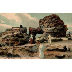 Carte postale ancienne colorisée de Biarritz montrant la Roche Percée à marée basse, voyagée en 1909.
