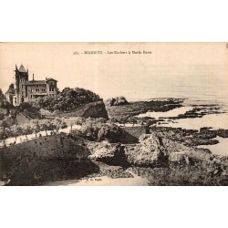 Carte postale ancienne de Biarritz montrant les rochers à marée basse et une villa dominant les falaises.