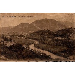 Carte postale ancienne de Lourdes montrant une vue générale de la ville et du Gave de Pau avec les Pyrénées en arrière-plan.