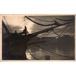 Carte postale ancienne montrant un voilier dans le port de Dunkerque au crépuscule avec les silhouettes des marins.
