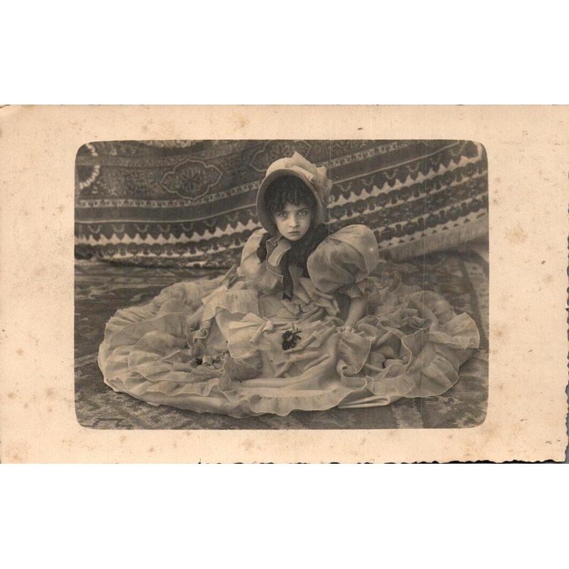 Carte postale photographique ancienne représentant le portrait d’une jeune enfant en robe de cérémonie avec chapeau.