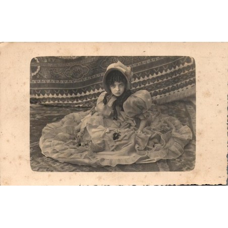 Carte postale photographique ancienne représentant le portrait d’une jeune enfant en robe de cérémonie avec chapeau.