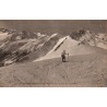 Carte postale ancienne de Superbagnères montrant un skieur face à la chaîne des Pyrénées enneigée.